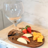 Wooden cutting board with fruit and cheese on a marble surface with a wine glass.