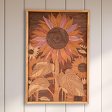 A framed wood art print of a large sunflower hangs on a light beige paneled wall above a white sofa with a green throw blanket in a bright, modern living room.