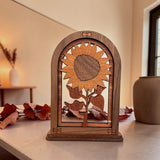 A wooden sunflower silhouette wall decor piece displayed on a tabletop in a warm, neutral-toned room.