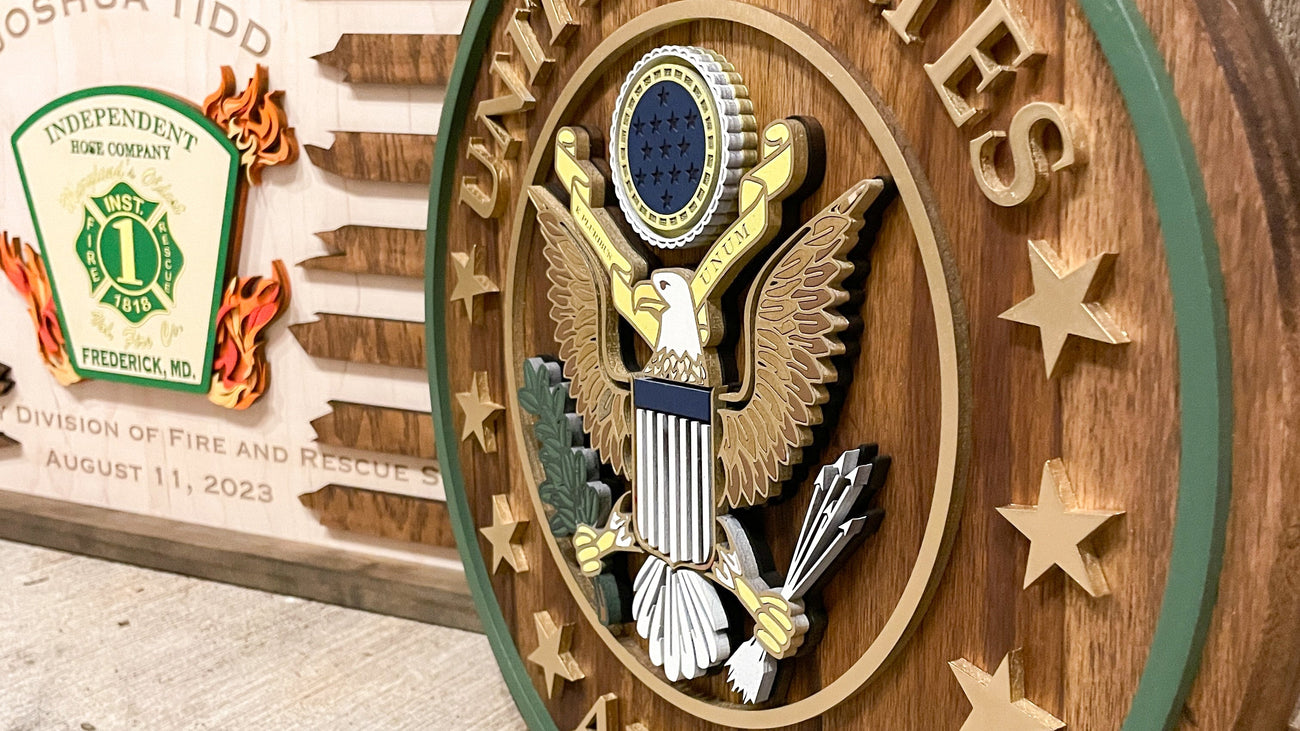 A round wooden United States Army seal plaque with a raised eagle emblem and gold lettering, displayed against a rustic wood background with another commemorative plaque partially visible behind it.