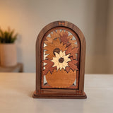 A small wooden decorative sculpture with an arched top and sunflower motif, displayed on a light beige tabletop with a softly blurred indoor background.